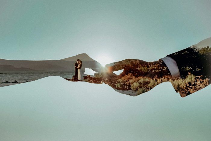 two hands holding each other in front of the ocean with trees and mountains behind them