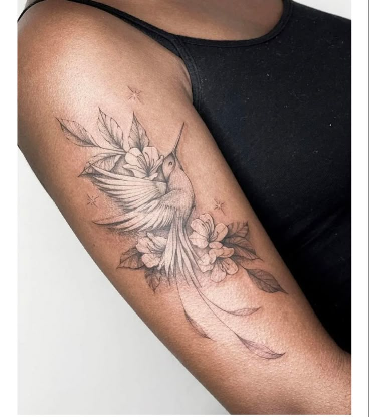 a woman's arm with a bird and flowers tattoo on the left side of her arm