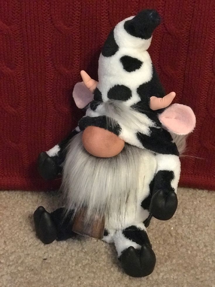 a stuffed cow sitting on the floor next to a red wall with its legs spread out