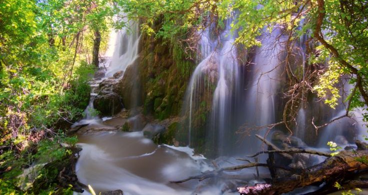 a waterfall in the middle of a forest with lots of water flowing down it's sides