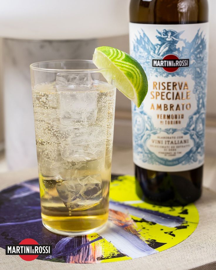 a bottle of beer next to a glass filled with ice and limes on a table