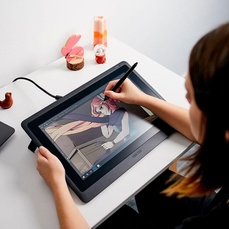 a woman sitting at a desk drawing on an electronic tablet with a pen and pencil