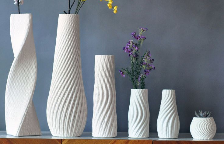 five white vases with flowers in them sitting on a shelf next to a wall