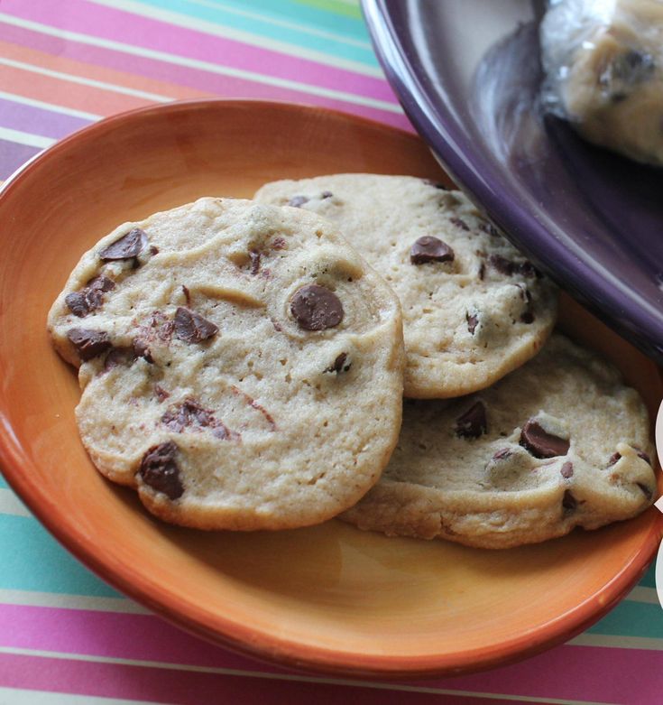 three chocolate chip cookies are on an orange plate next to a bowl of ice cream