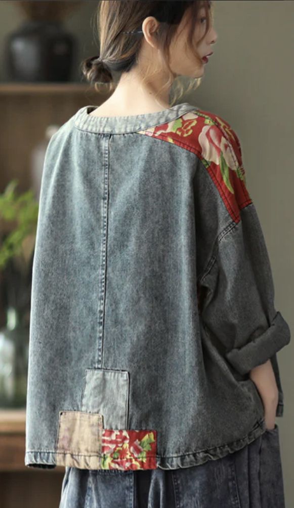 a woman standing in front of a wall wearing a jean jacket with flowers on it