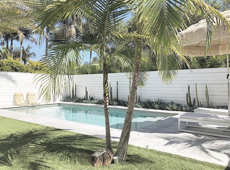 a pool surrounded by palm trees next to a white fence and grass covered lawn area