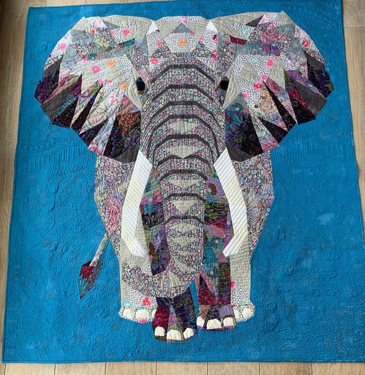 an elephant made out of patchwork on a blue rug with wood flooring in the background