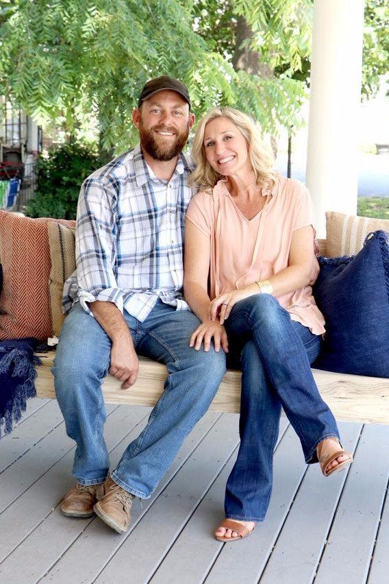 a man and woman are sitting on a porch swing smiling at the camera while posing for a photo