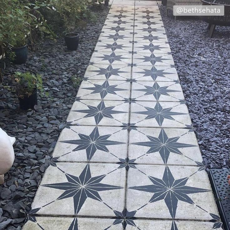 a walkway made out of cement with black and white star designs on the ground next to potted plants