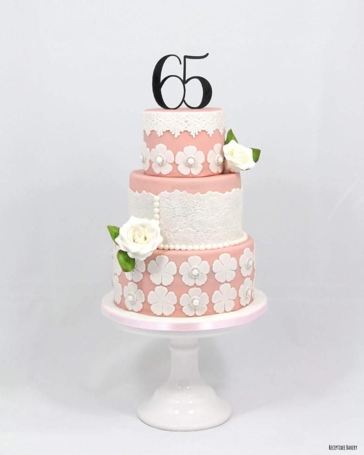 a pink and white wedding cake with flowers on the bottom tier is decorated with black number 65