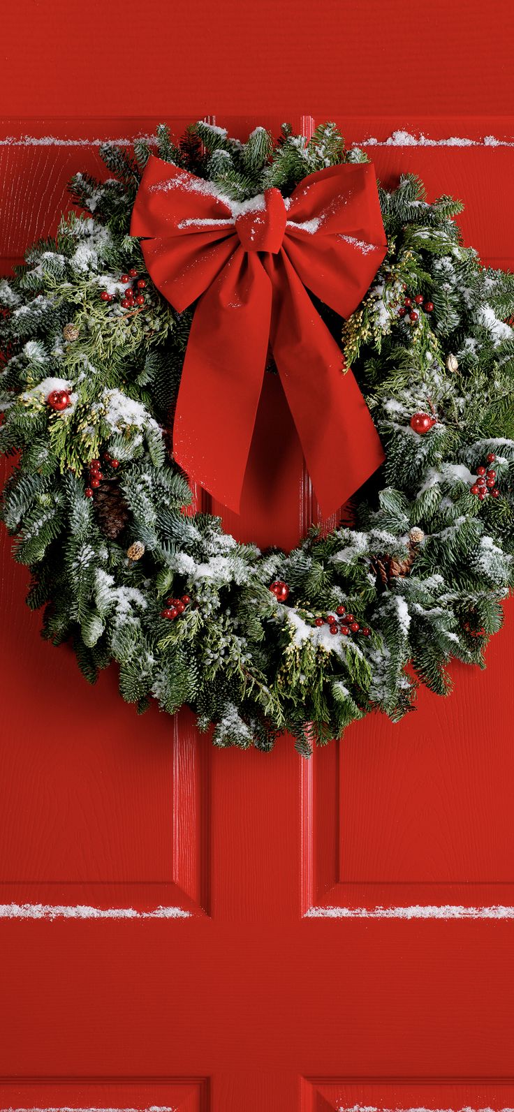 a christmas wreath on a red door with a bow hanging from the front and side