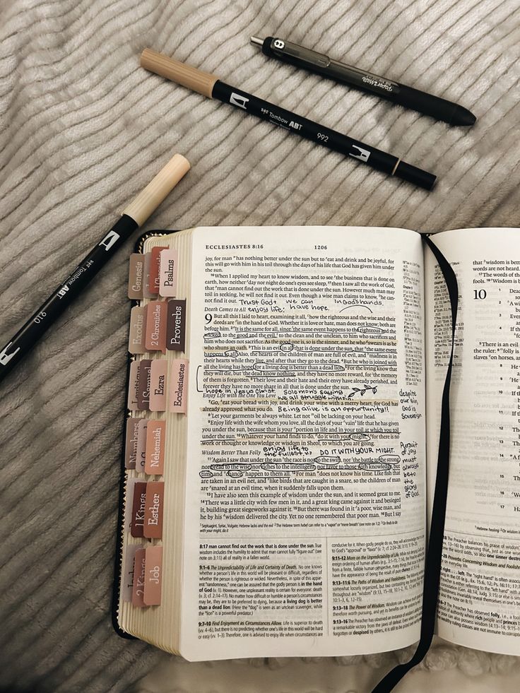 an open book with writing utensils next to it on top of a bed