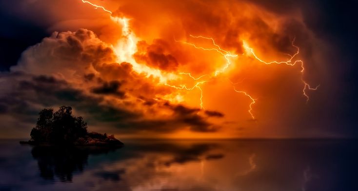 an orange and red cloud with lightning in the sky above it, reflecting on water