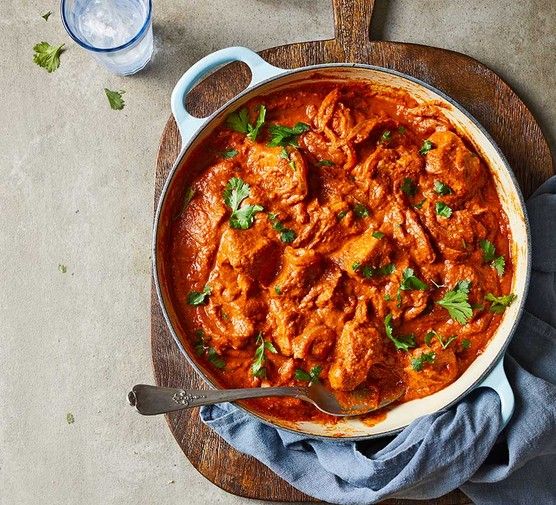 a large pot filled with meat and sauce on top of a wooden cutting board next to a glass of water