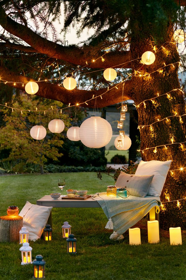 an outdoor dining area with lanterns strung from the tree and lights on the branches above it