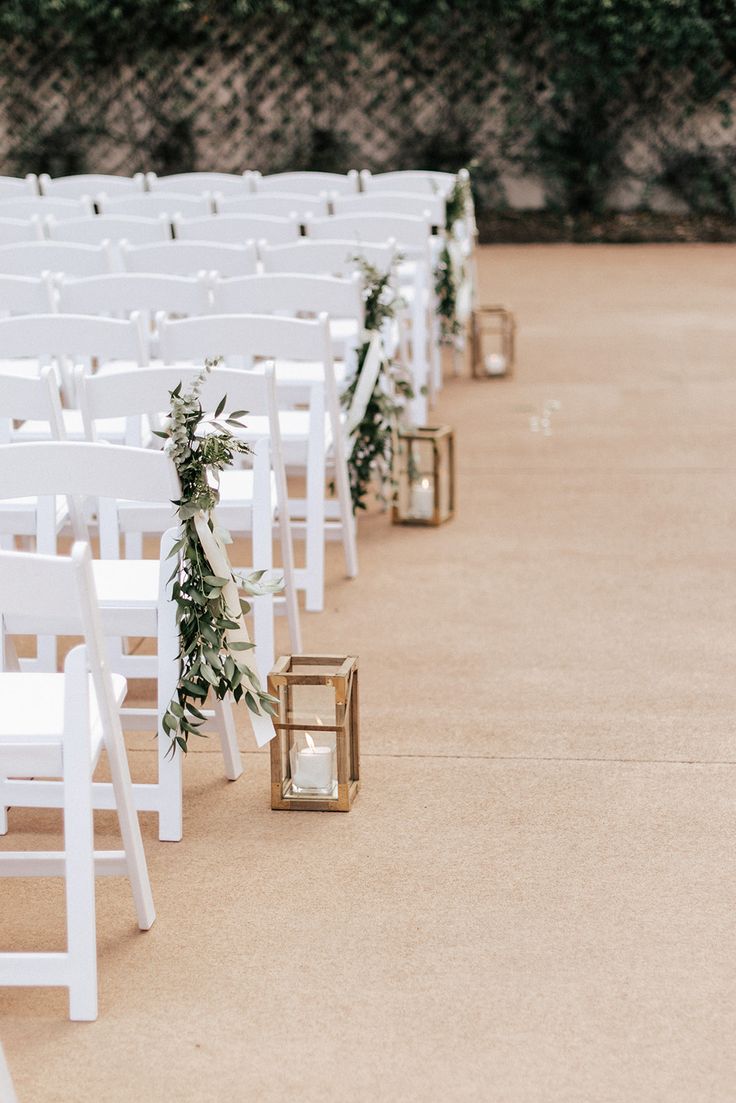 rows of white chairs with greenery and candles on the aisle for an outdoor ceremony