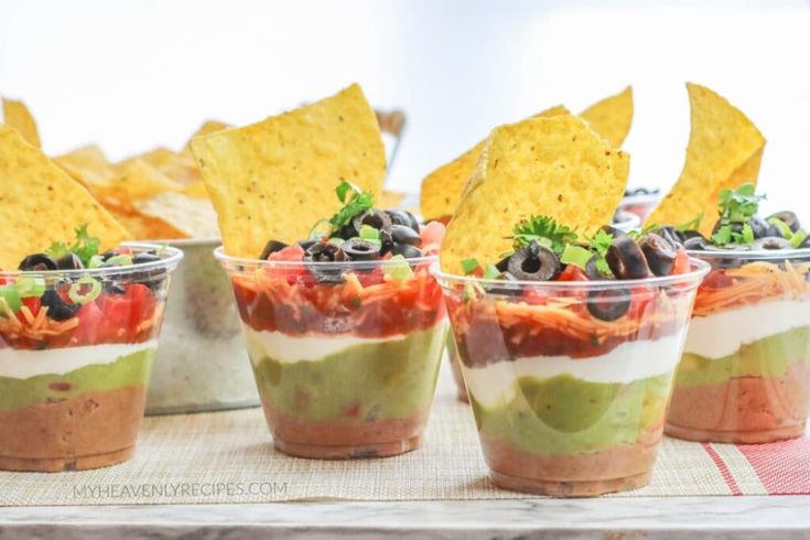 three cups filled with food and chips on top of a wooden tray next to each other