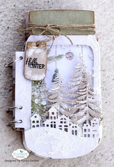 an altered christmas card with white paper and trees in the snow, on top of a concrete surface