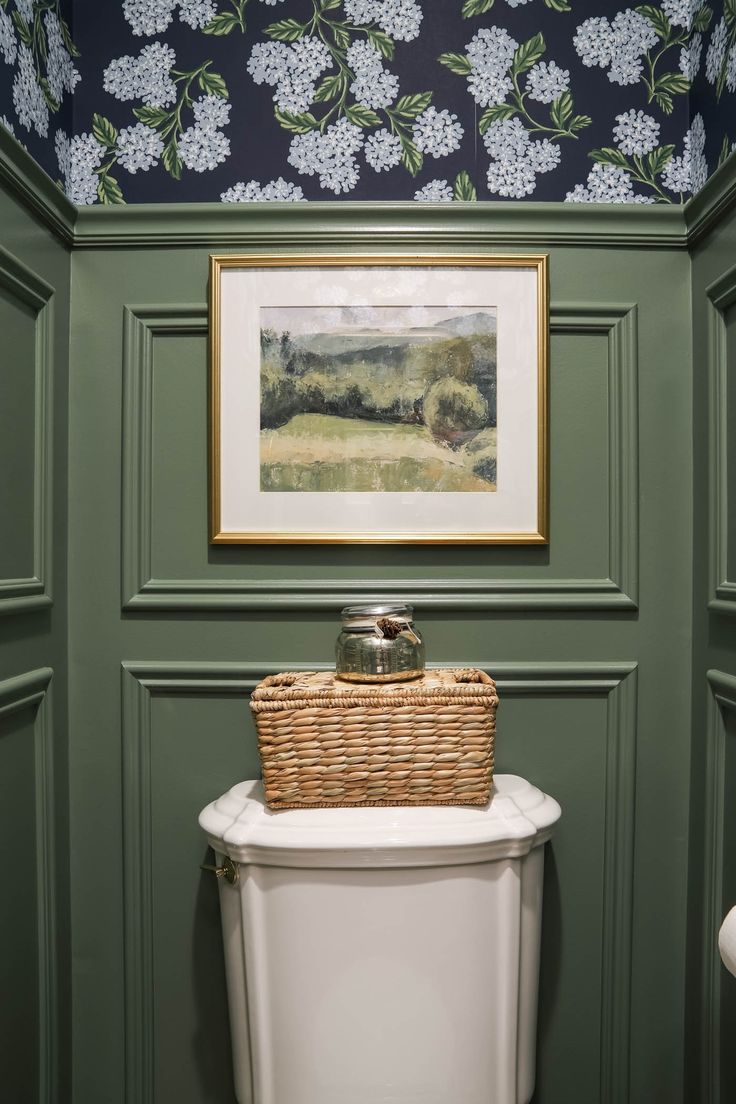 a bathroom with green walls and a painting on the wall above a white toilet bowl