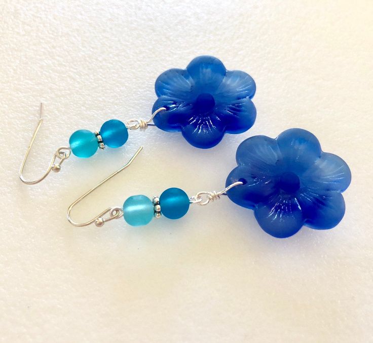 "Beautiful light sapphire blue or royal blue sea glass flowers are the feature of these pretty dangle earrings. Large 1\" sea glass flower is accented with contrasting shades of royal blue, teal and aqua blue sea glass rounds. Earrings are made of cultured tumbled sea glass and wire wrapped in German silver plated jeweler's wire. They hang from silver plated ear wires. Light sapphire blue earrings measure 2\" long and royal blue are 2 1/4\" long. Also available in Sterling silver. Listing is for Blue Flower Charm Drop Earrings, Blue Flower Earrings Nickel Free, Blue Flower-shaped Jewelry For The Beach, Blue Flower Jewelry For The Beach, Blue Sea Glass Nickel Free Earrings, Blue Sea Glass Nickel-free Earrings, Blue Recycled Glass Dangle Earrings, Nickel-free Blue Sea Glass Earrings, Blue Flower Earrings For Jewelry Making