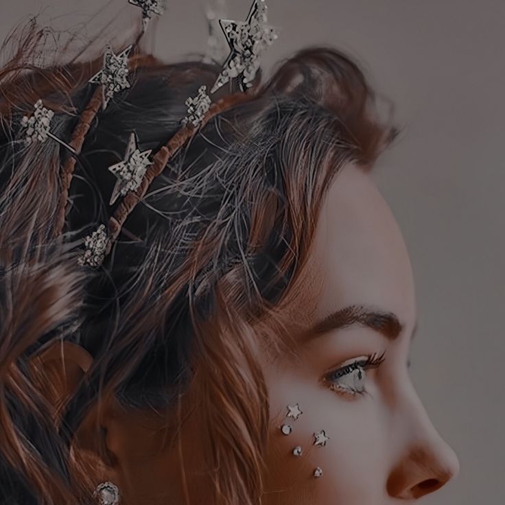 a woman with stars on her face is wearing a tiara and looking off into the distance