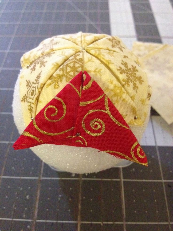 an ornament on top of a white ball with red and gold fabric in the shape of a triangle