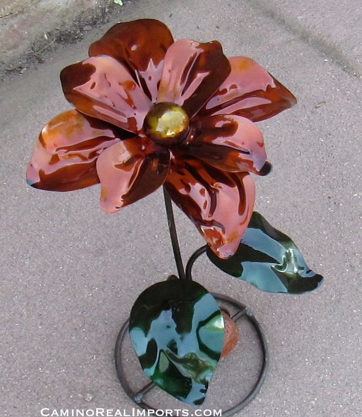 a glass flower sitting on top of a metal stand in the middle of concrete ground