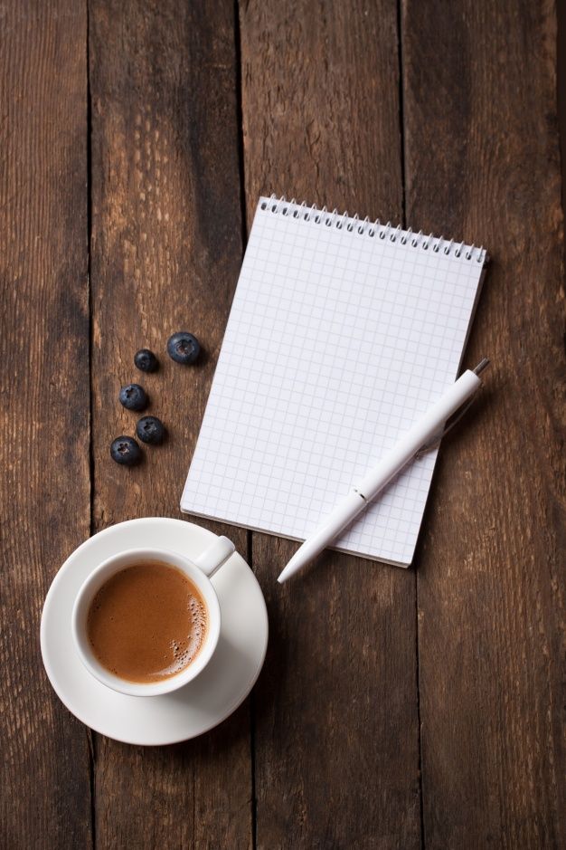 a cup of coffee next to a notepad and some blueberries