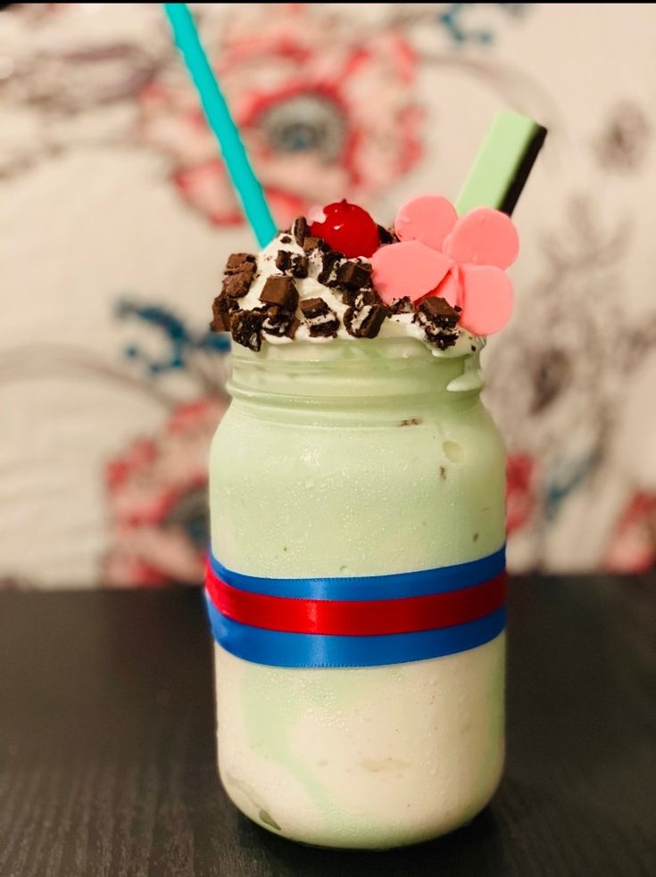 a green drink with whipped cream, chocolate chips and cherries on top is sitting on a table