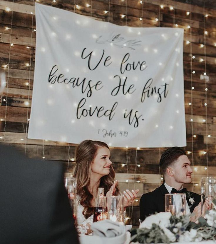 two people sitting at a table in front of a sign that says we love because he first loved us