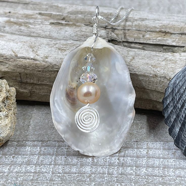 This beautiful pendant is made from a natural white oyster shell found on the beaches in the Cape May area. A spectacular metallic fresh water pearl is nestled inside the oyster shell showing off the treasure inside. The shell was then wire wrapped with sterling silver wire. The pendant measures 2 inches in length from the top of the bail and 1 inches wide. The pendant is on a 16" sterling silver box chain but other lengths are available in the below options. Silver Shell With Pearl Pendant, Silver Shell Necklace With Pearl Pendant, Silver Shell Jewelry With Pearl Charm, Silver Pearl Shell Necklace, Silver Pearl Shell Necklace Gift, Silver Pearl Shell Necklace As A Gift, Silver Pearl Shell Necklace For Gift, Silver Mother Of Pearl Shell Gift, Handmade Silver Shell Pendant