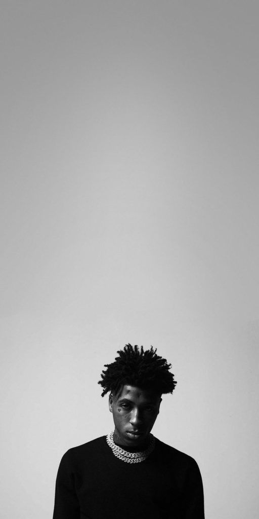 a young man with dreadlocks standing in front of a white wall and looking at the camera