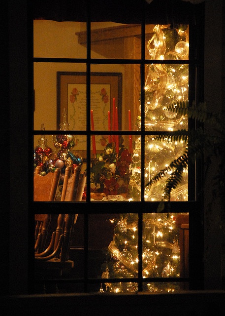 a lit christmas tree is seen through an open window