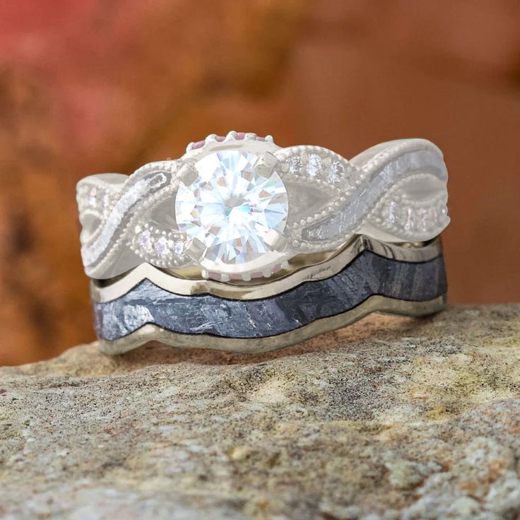 two wedding bands with a diamond in the center on top of a stone surface next to a rock