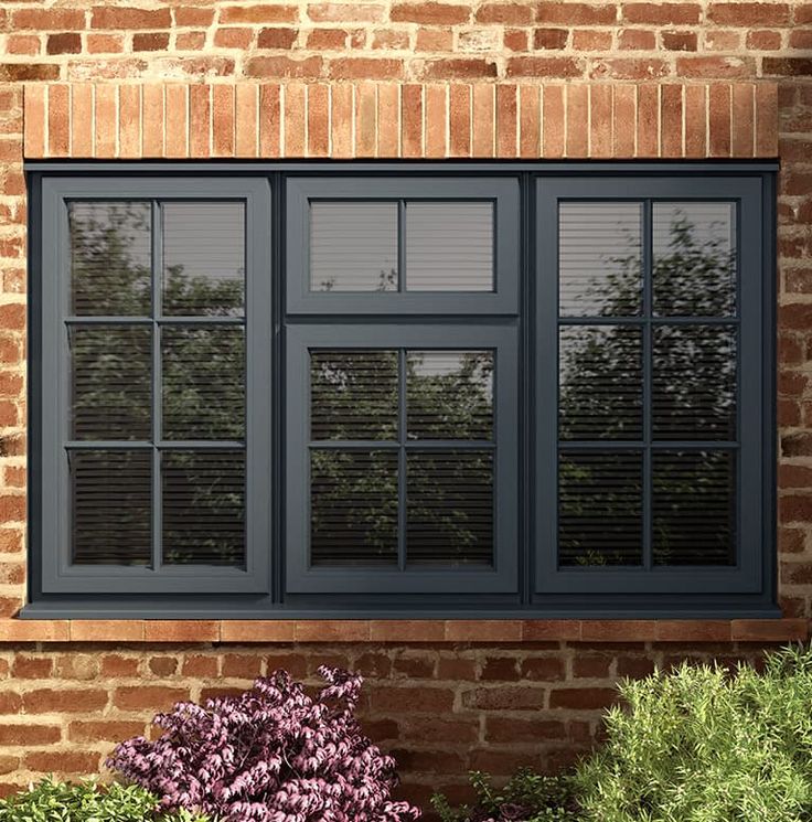 a brick building with two windows and plants in the foreground, one window is closed