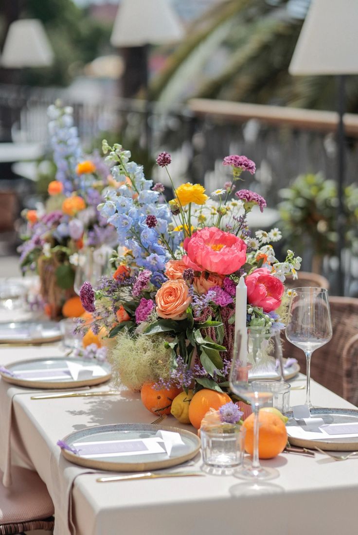 a vase filled with lots of colorful flowers on top of a table next to wine glasses