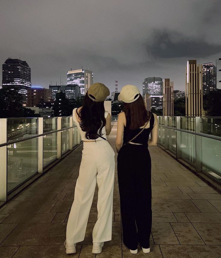 two women are standing on a bridge looking at the cityscape in the distance