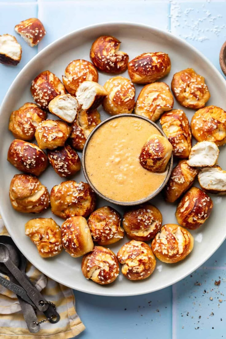 a white plate topped with pastry covered in cheese and dipping sauce next to utensils