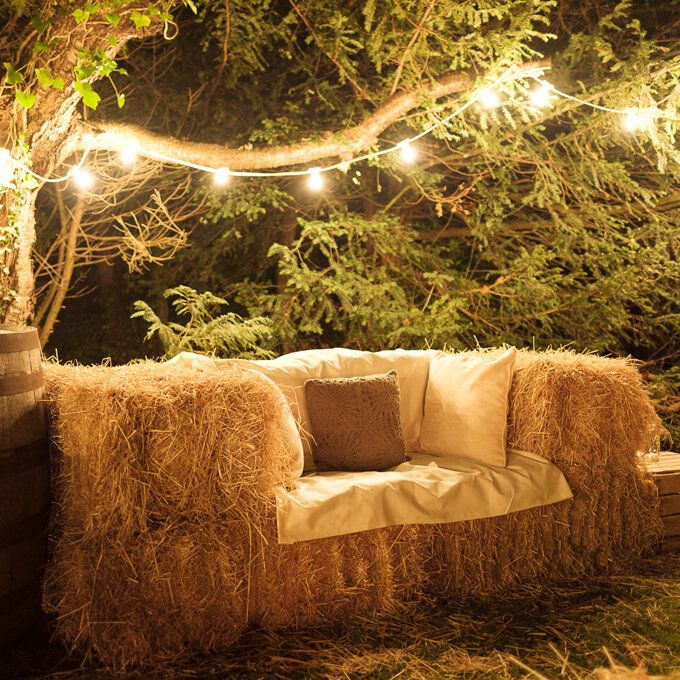 a couch made out of hay sitting under a tree with string lights strung over it