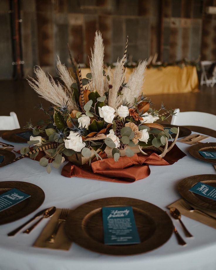 the table is set with plates and silverware, flowers and greenery on it