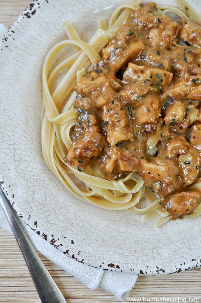 a white plate topped with pasta and meat covered in sauce on top of a wooden table