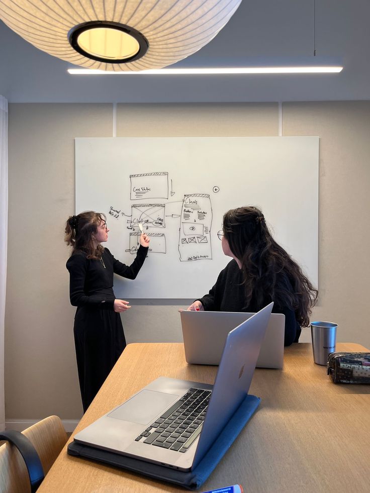 two women standing in front of a whiteboard with laptops on it