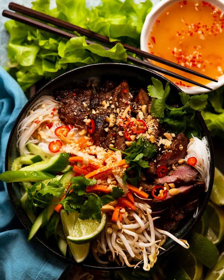 a bowl filled with meat and veggies next to chopsticks on a blue cloth