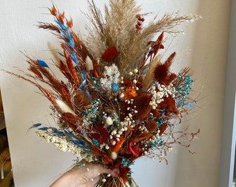 a hand holding a bouquet of dried flowers