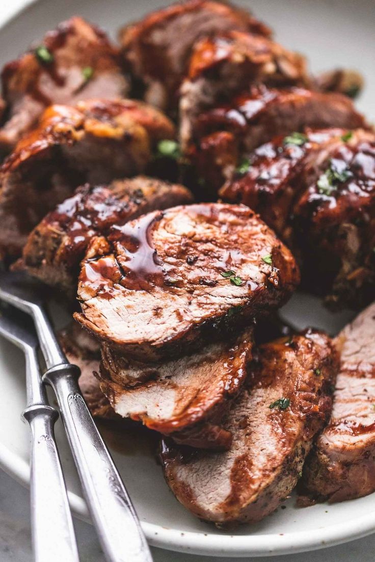 some meat is on a plate with tongs and a fork next to the food