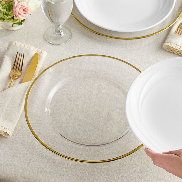 a person holding a white plate with gold trim around it on top of a table