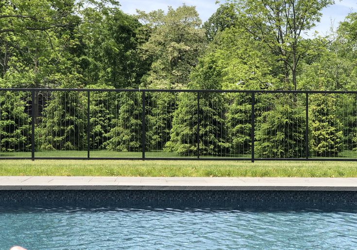 a pool with a fence surrounding it and some trees in the back yard behind it