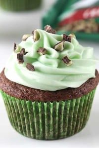 a chocolate cupcake with green frosting and nuts on top, next to a bag of cookies