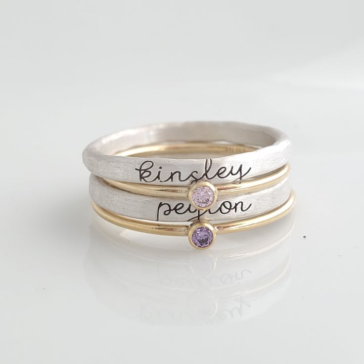 Cursive Name Stackable Birthstone Ring Set This set includes four rings! You will receive two name rings in fine silver (.999) engraved in our cursive font. These tarnish much slower than sterling silver since they have less copper. You will also receive two skinny cz birthstone rings in 14K yellow gold filled. These rings are handmade in our Indiana studio. Each engraved ring starts from a spool of wire. They are handcut, handformed and soldered in the first process of creating your ring. They Name Rings Personalized, Stackable Name Rings, Stackable Birthstone Rings, Birthstone Stacking Rings, Birthstone Rings, Name Ring, Cursive Font, Mother Rings, Basic Jewelry