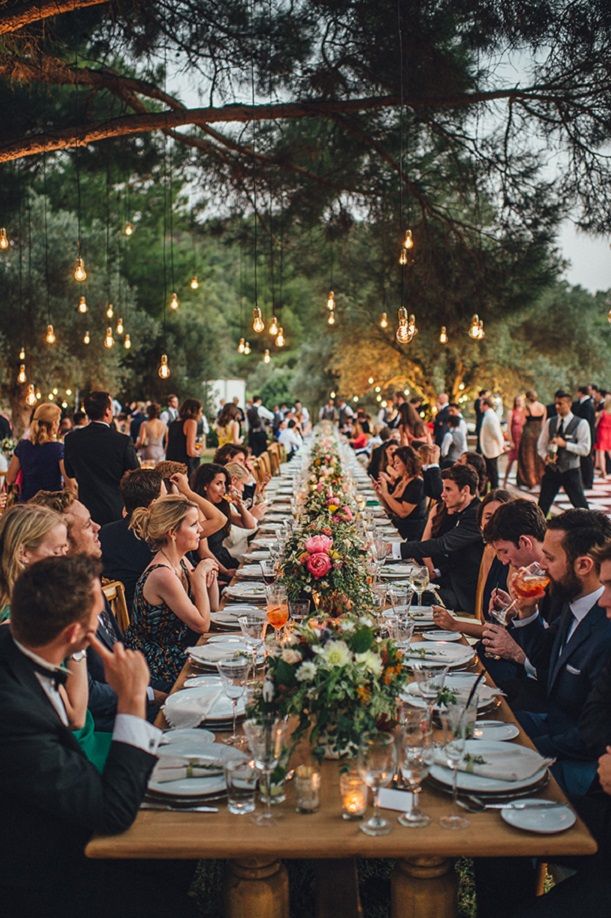 a group of people sitting around a long table with plates and glasses in front of them